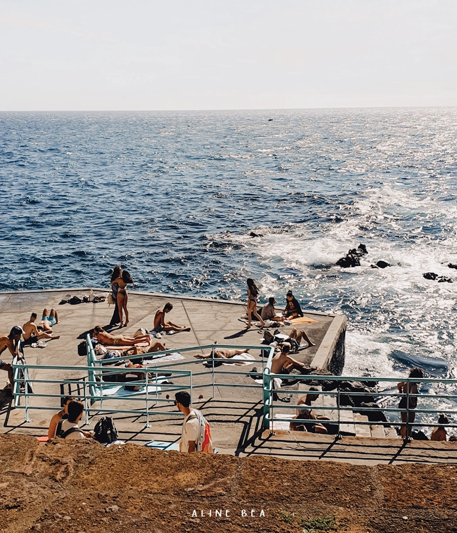 People sunbathing on a concrete platform by the sea.