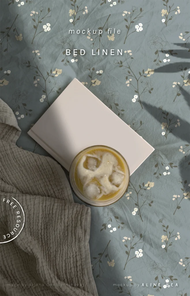 A section of a bed showing a floral sheet, a notebook and a glass of iced coffee on top of the notebook.