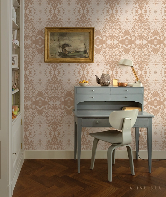 Living room scene displaying an antique wooden workstation with a lamp and wooden chair, in front of a wall with a decorative wallpaper by Aline Bea. A section of a wooden book shelf appears on the left of the image.
