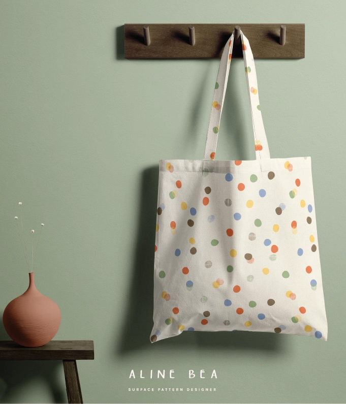 A tote bag hanging on a wooden hanger fixed on the wall. The tote bag has a polka dot pattern from celebrate collection by Aline Bea