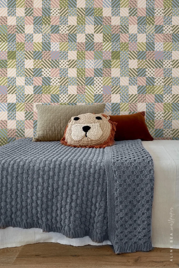 Pastel patchwork plaid wallpaper in green, blue, and pink behind a children's bed