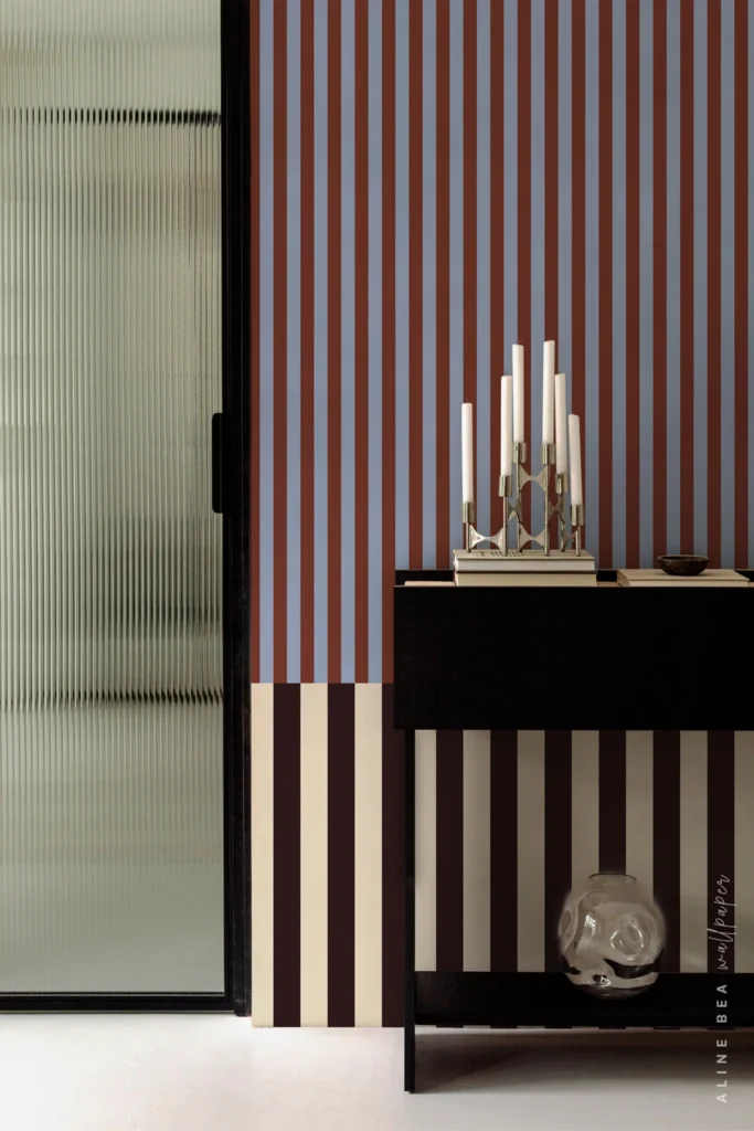 Rust and periwinkle blue striped wallpaper with a maroon and cream border behind a console table in a contemporary hallway. Shop wallpaper.