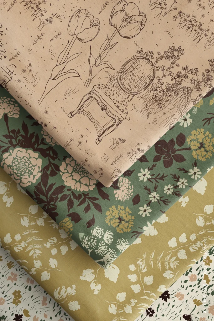 Five fabric swatches folded and stacked diagonally: a blush pink toile de jouy with a hand-drawn line illustration of a tulip, an armchair, and wildflowers on top, a sage green floral with many blooms and leaves beneath it, a mustard yellow fabric scattered with small white leaves, and a cream fabric with expressive brush strokes resembling little florals in a wild grassland at the bottom.