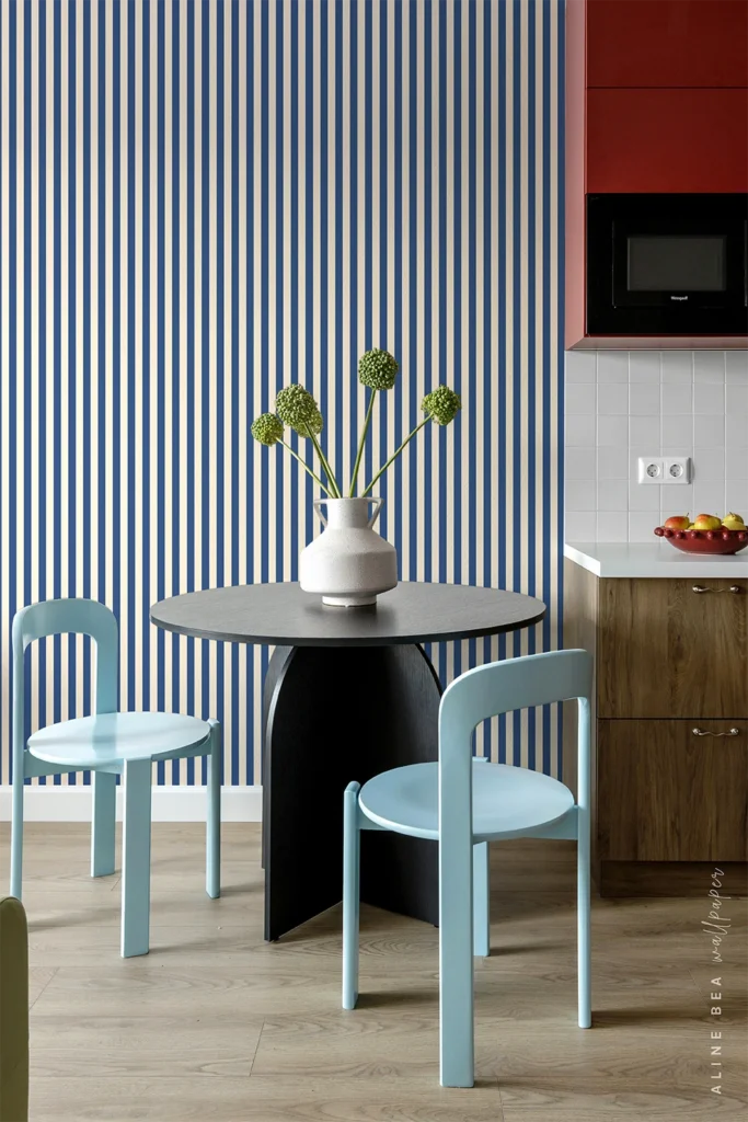 Navy blue and white narrow-striped wallpaper behind a round black dining table and light blue chairs in a small kitchen