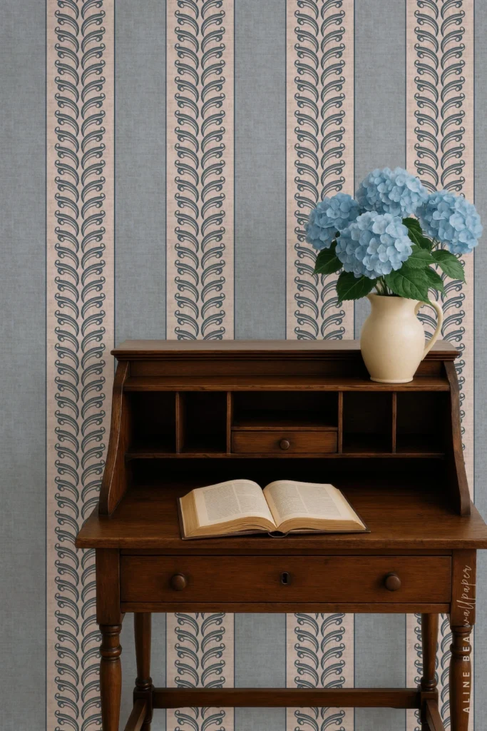 Dusty blue linen-textured wallpaper with cream stripes of navy leaf ornaments behind an antique wooden writing desk