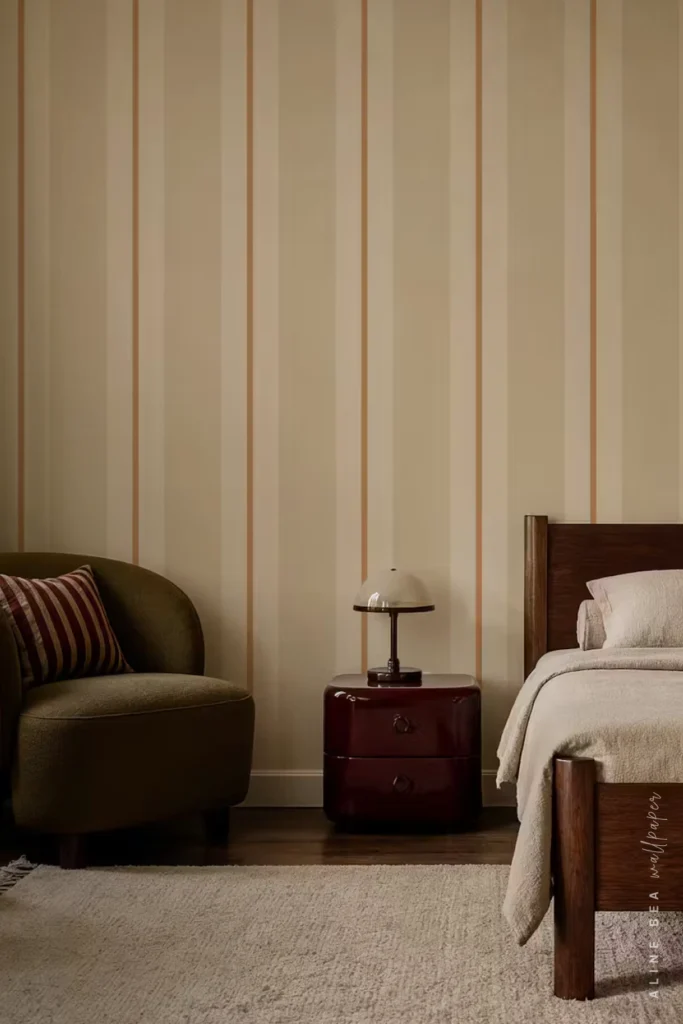 Cream and beige wide-stripe wallpaper with thin caramel pinstripes in a bedroom with an olive armchair and burgundy nightstand