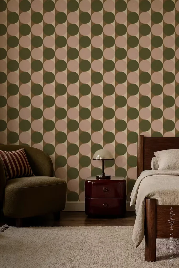 Olive green and blush pink geometric wallpaper of overlapping half-circles in rows behind an olive armchair and burgundy nightstand