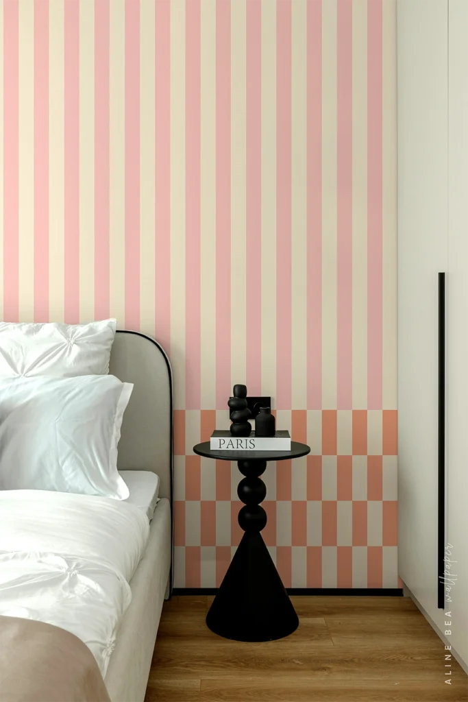 Pink and cream striped wallpaper above a coral and cream checkerboard band behind a black sculptural side table in a bedroom